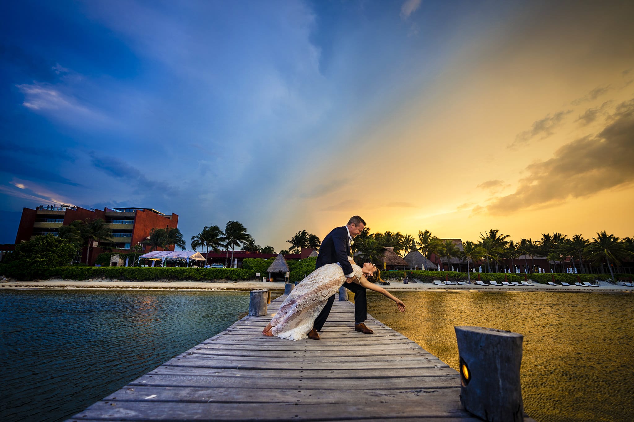 Groom dipping bride on dock at sunset