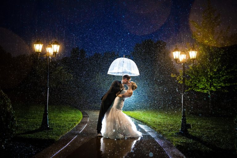 Husband and wife kiss in the rain underneath an umbrella at night at Cincinnati Wedding Venue the Manor House by Cincinnati Wedding Photographer Studio 22 Photography