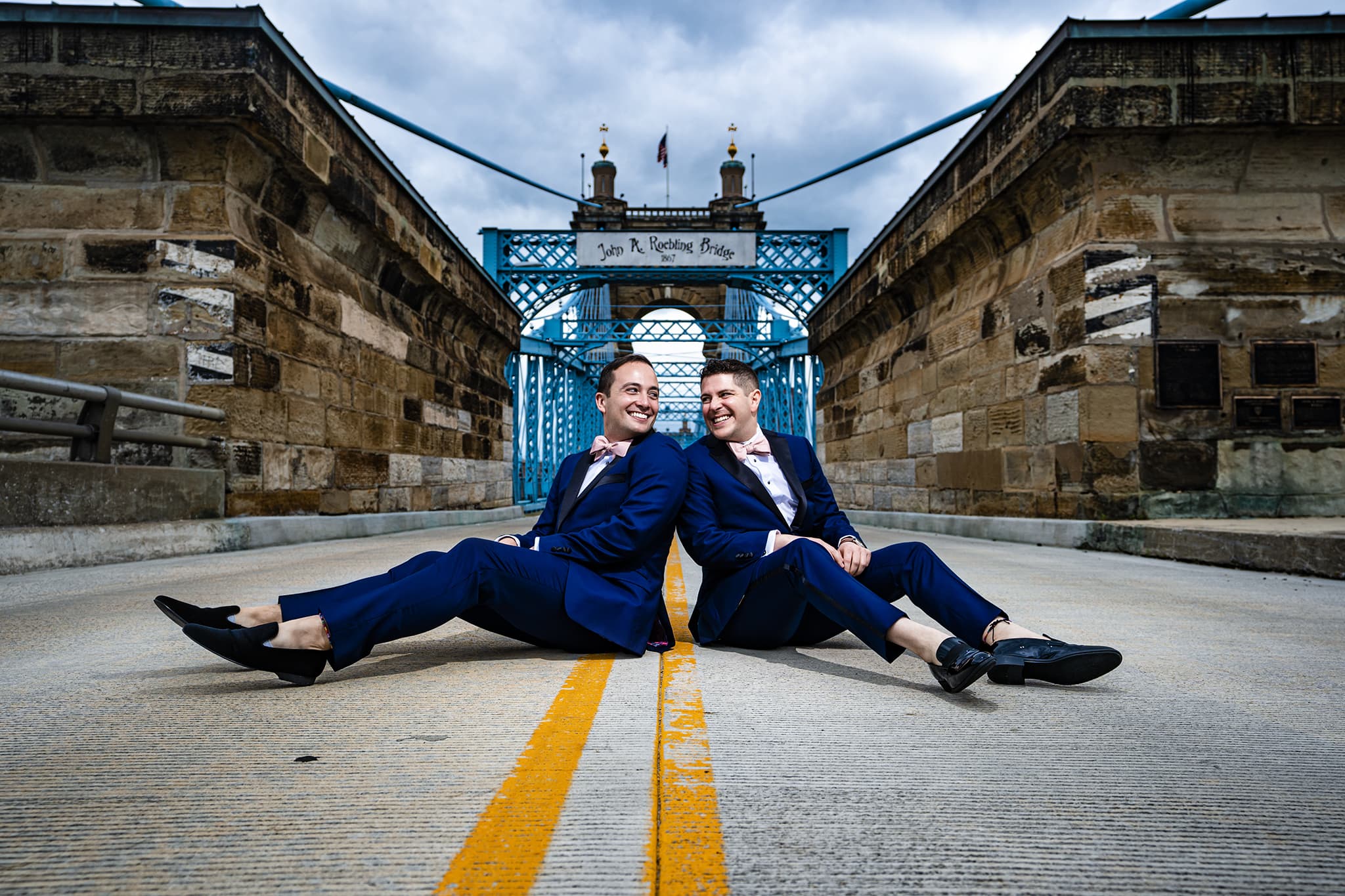 Two grooms sit on the Roebling Bridge in Cincinnati, Ohio before their Jewish wedding ceremony at the Renaissance Hotel in downtown Cincinnati. Photo by Studio 22 Photography